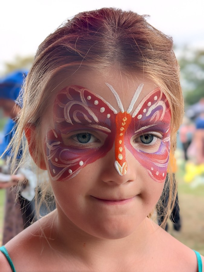 Child with a red and pink butterfly mask face painting with white swirls