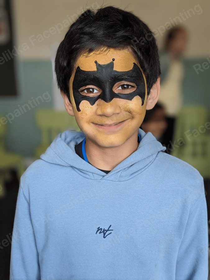 Smiling child with a black and gold bat hero mask face painting