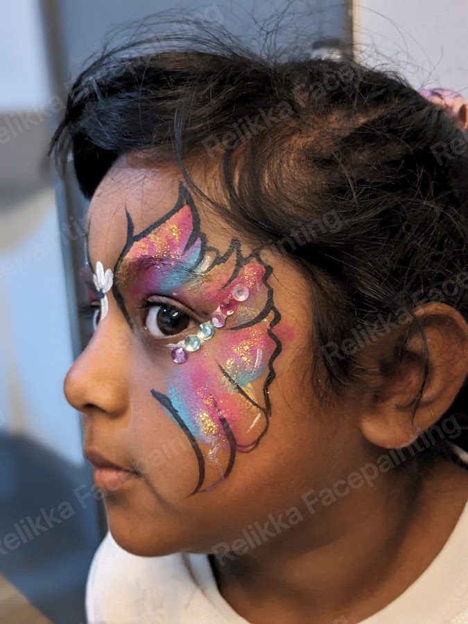 Child with a pink, blue and gold butterfly face painting decorated with gems