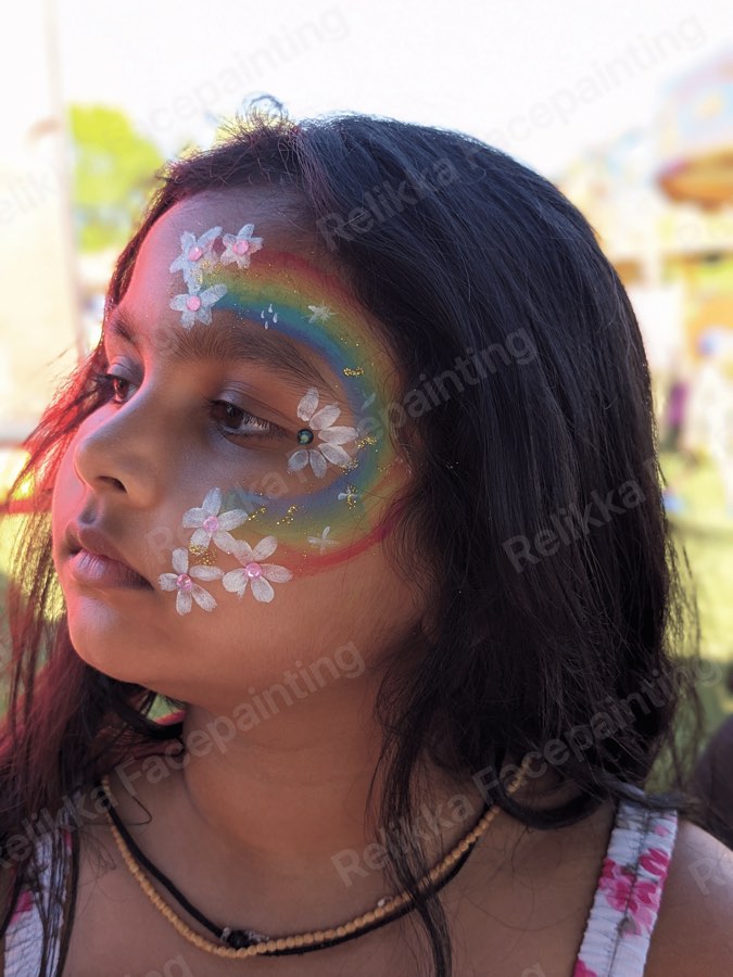 Child with a rainbow face painting decorated with white flowers