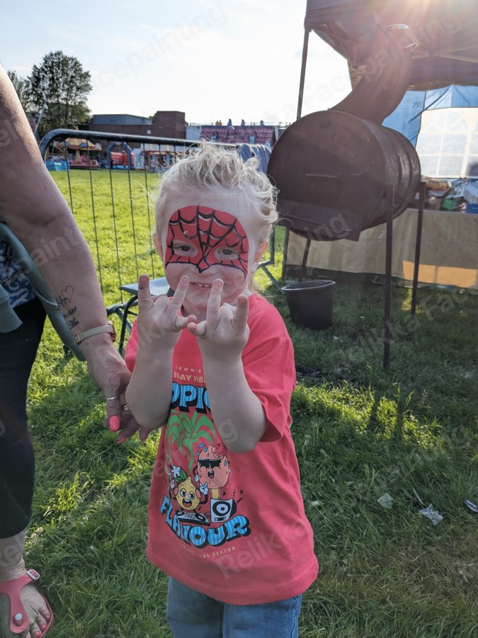 Toddler with a full red spider hero face painting at an outdoor fun day