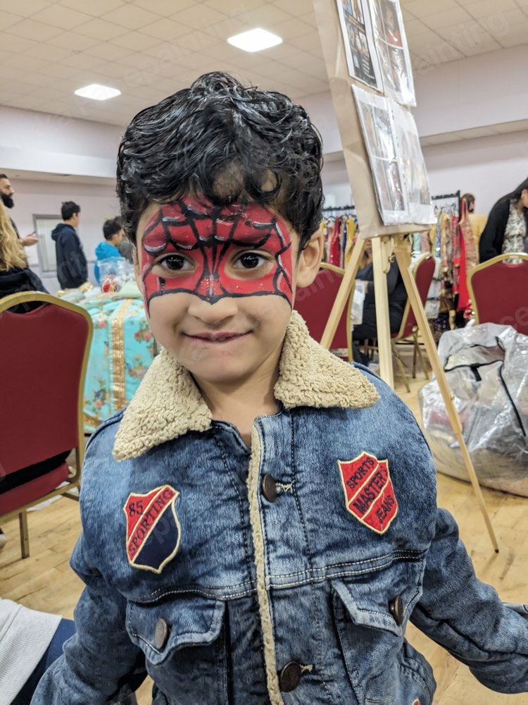 A child with a red spider hero mask face painting at an indoor community event