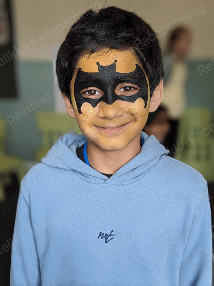 A smiling child with a black and gold bat hero mask face painting